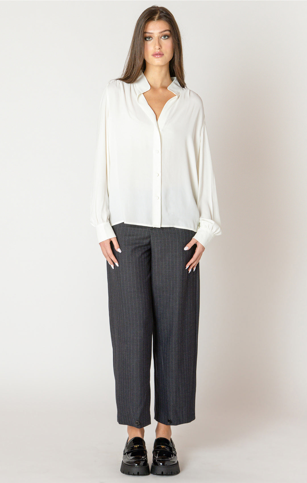 Woman wearing a white blouse and gray pants on a plain background